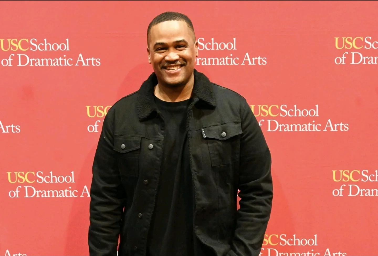 E'Ian West smiling at the USC School of Dramatic Arts event backdrop