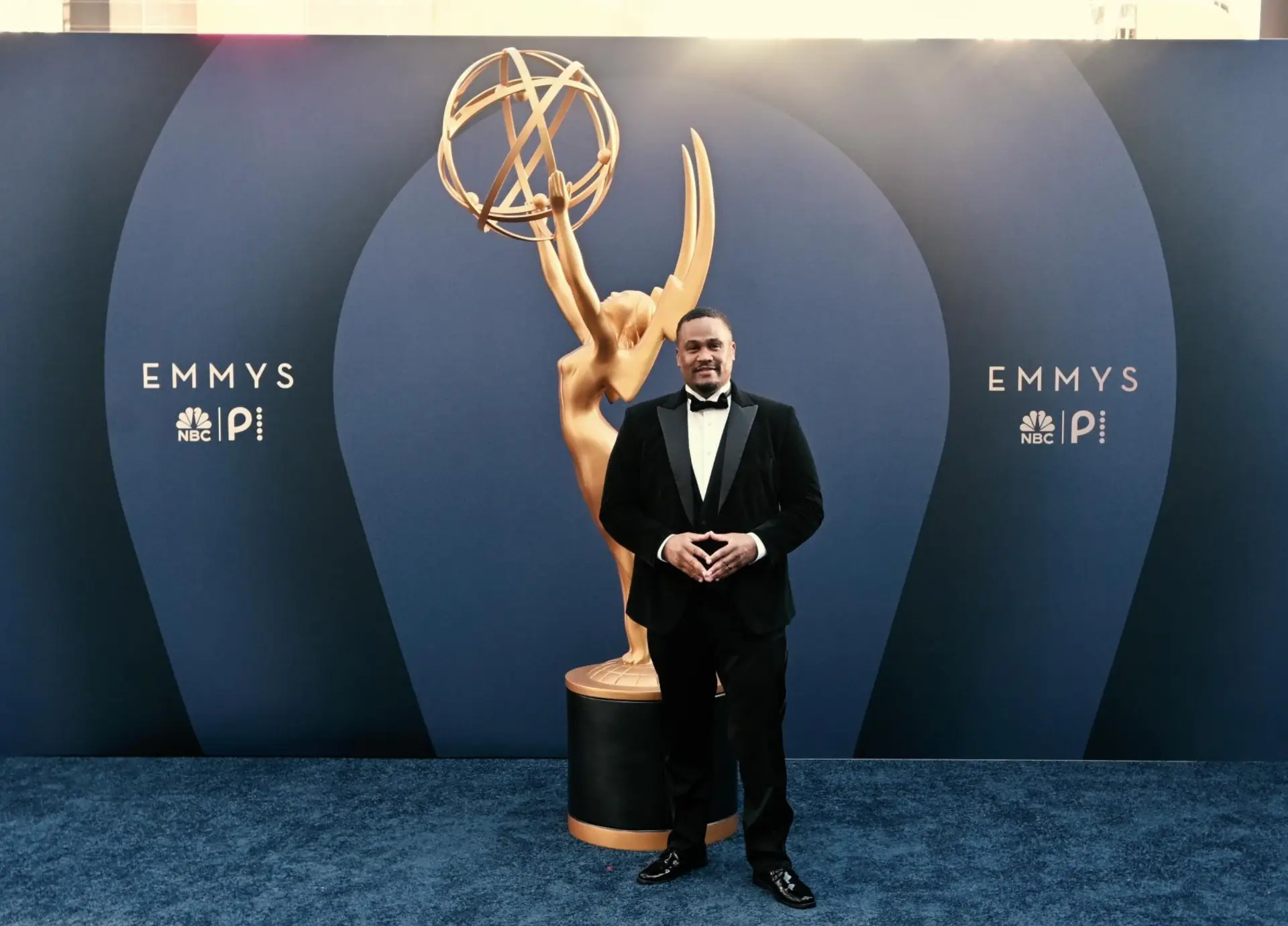 E'Ian West in a tuxedo beside the Emmy statue on the Emmys red carpet at the NBC and Peacock step and repeat