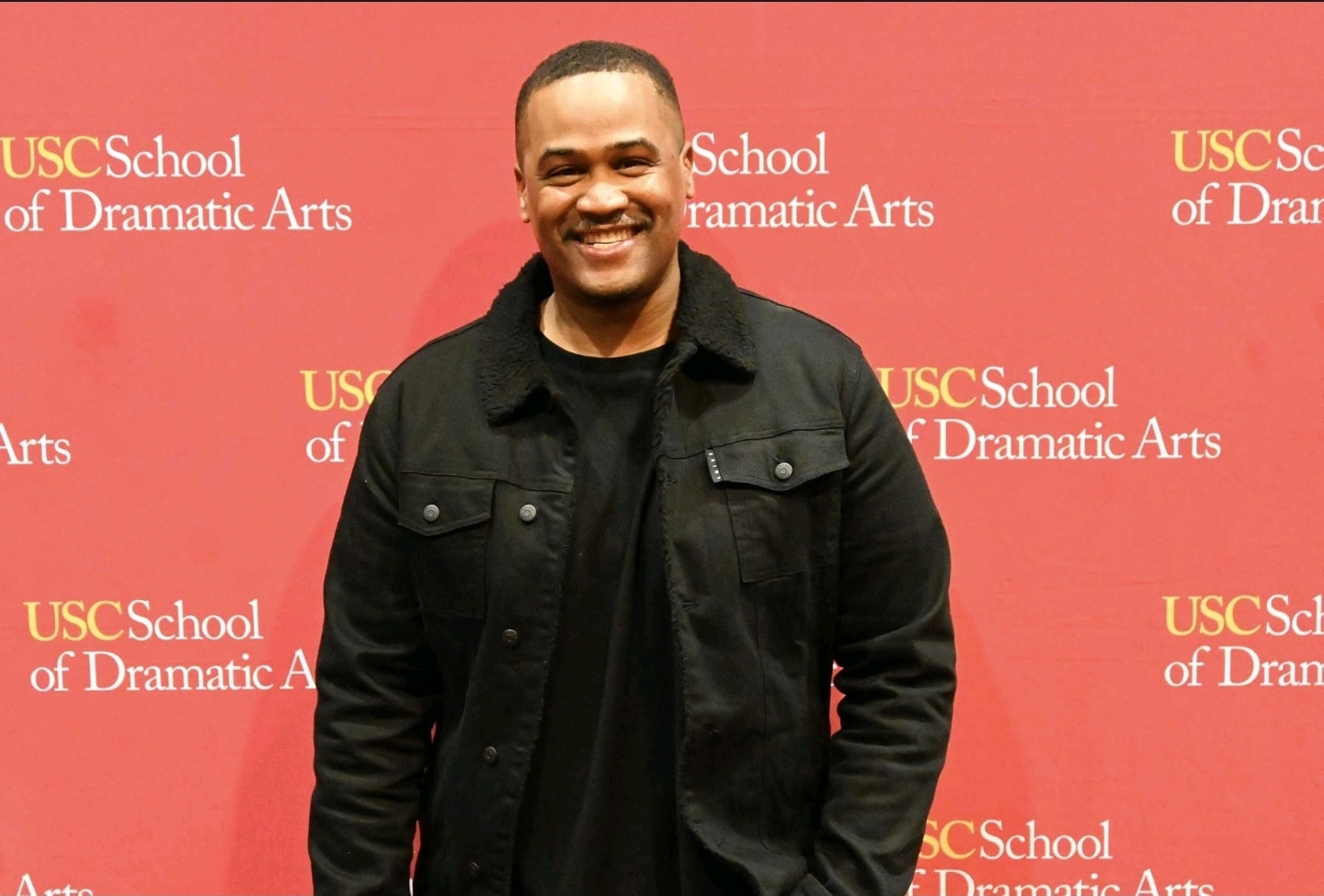E'Ian West smiling at the USC School of Dramatic Arts event backdrop