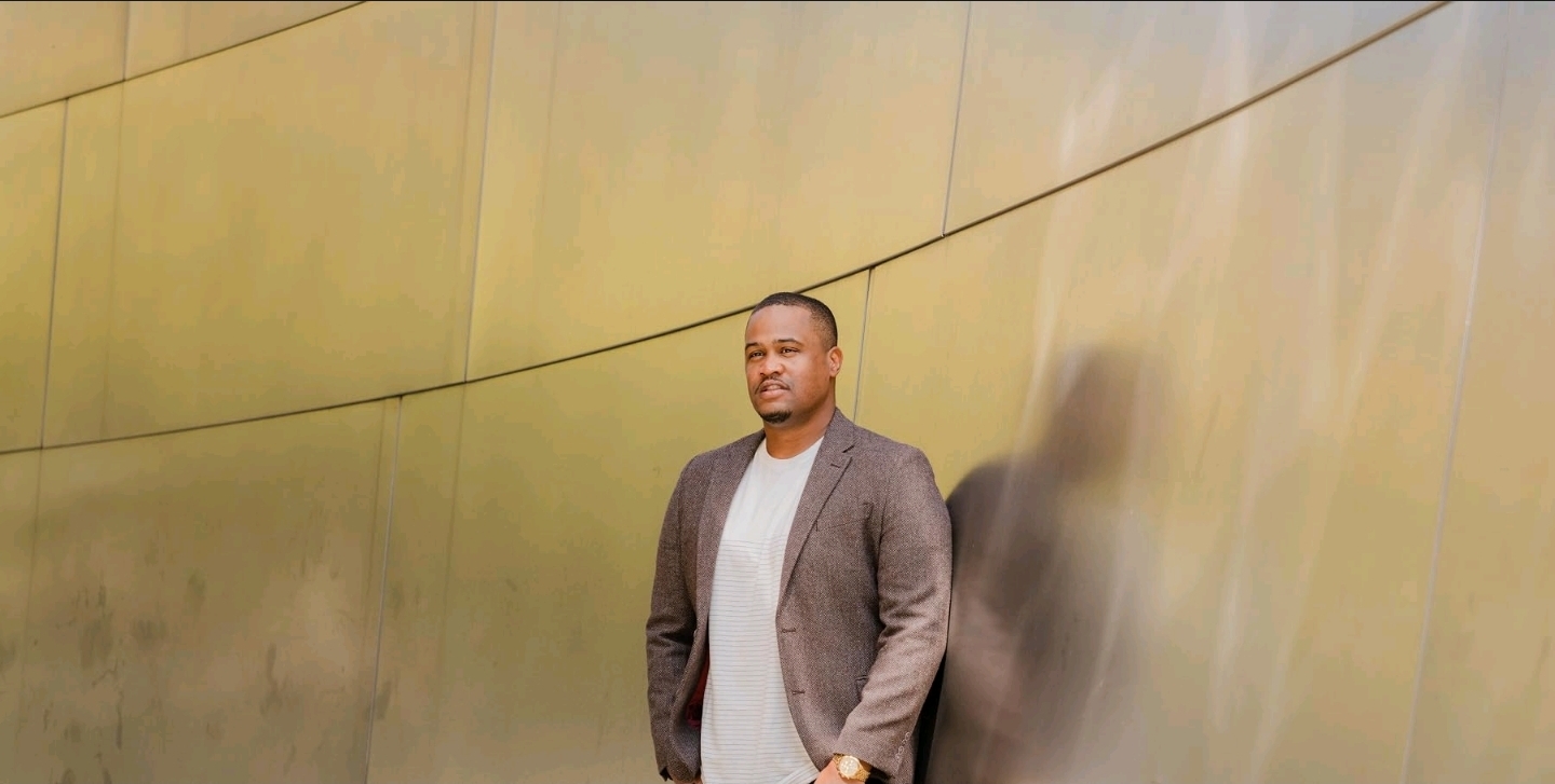 E'Ian West standing against a sculptural gold wall portrait backdrop